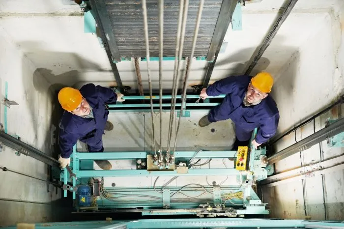 16404884_l-machinists-adjusting-lift-in-elevator-hoist-way–e1786507129290